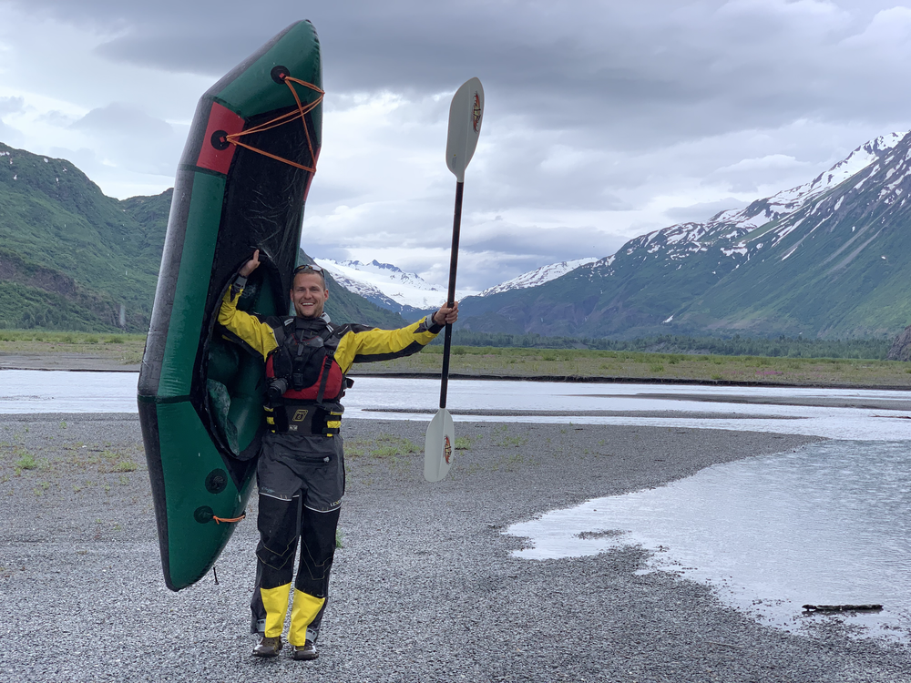 Guest holds boat and oar while enjoying a packrafting adventure in Alaska